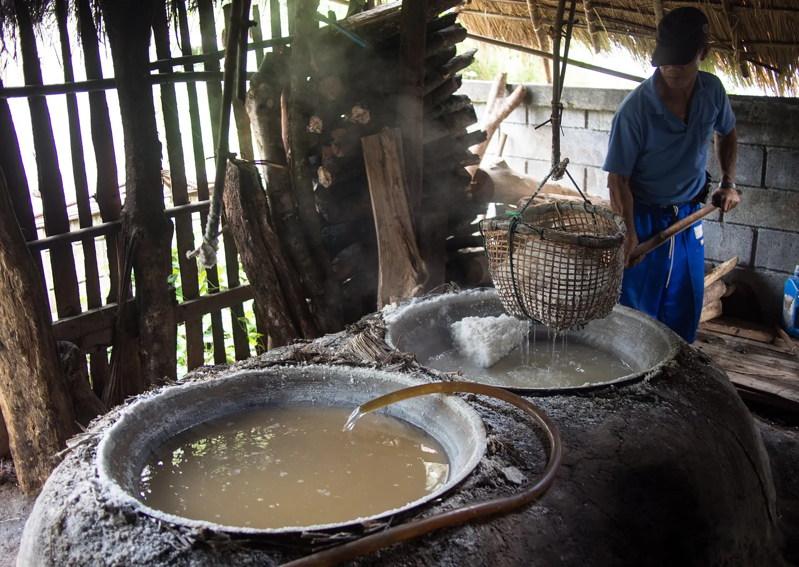 A man tending steaming pans of brine in a wooden salt house at Bo Kluea