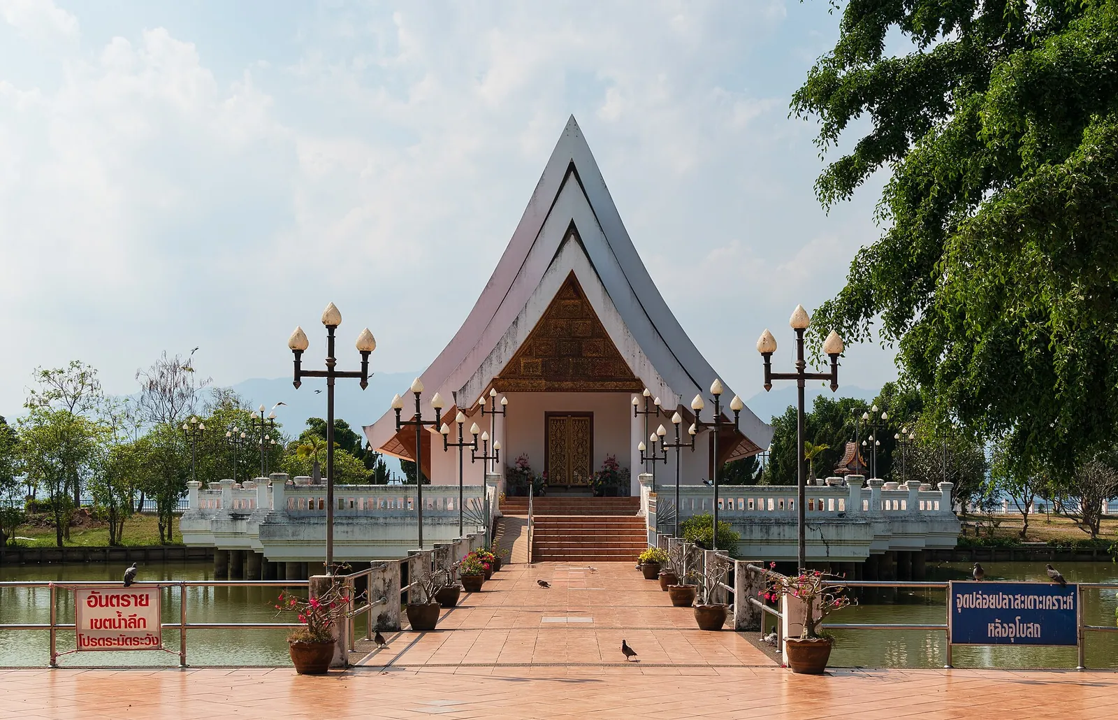 A sala de ordenação de telhado inclinado do Wat Si Khom Kham, a que se chega por um passadiço sobre a água