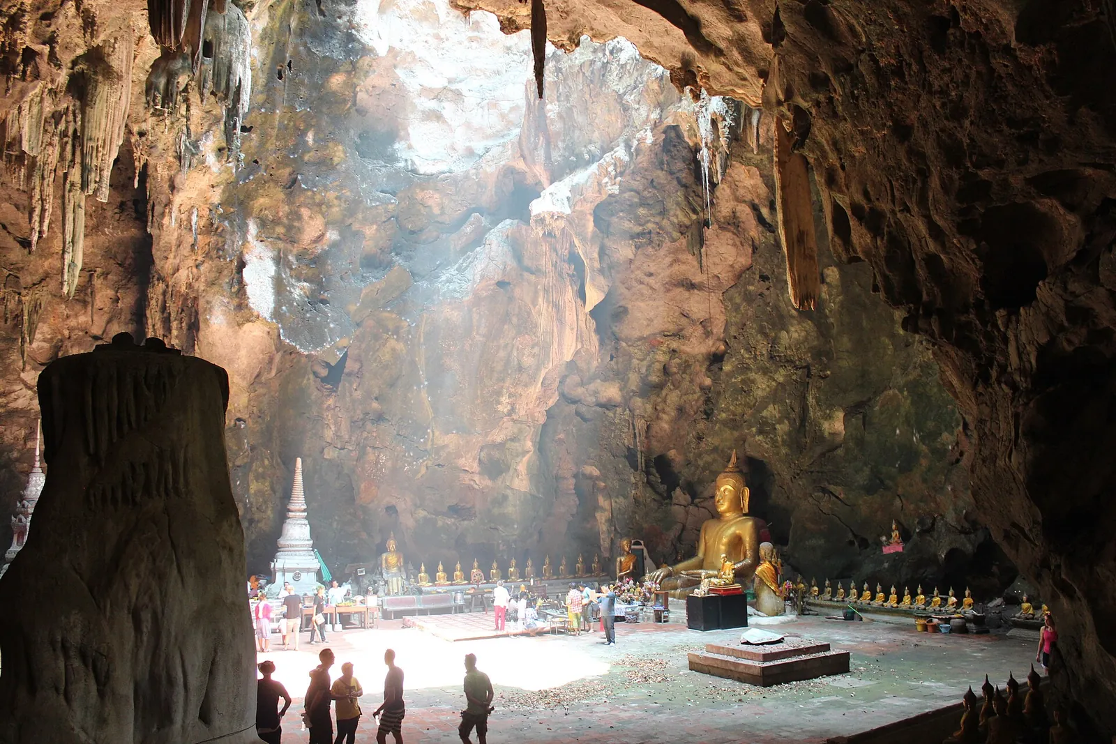 Shafts of sunlight falling through the roof of Tham Khao Luang onto Buddha images