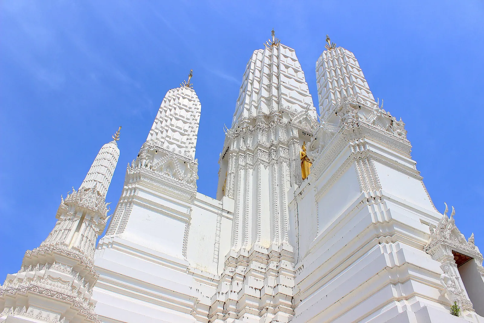 The tall white prangs of Wat Mahathat Worawihan against a bright blue sky