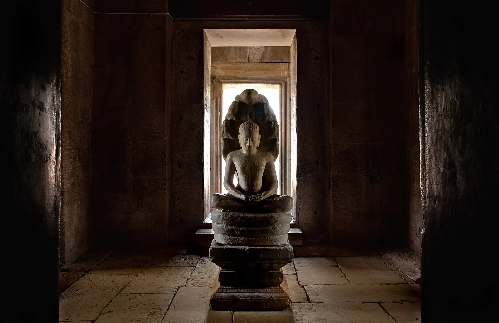 A Buddha image seated on a coiled naga inside a dark stone sanctuary doorway