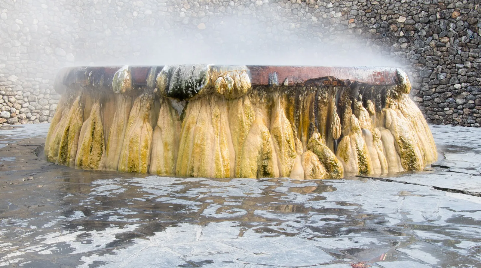 Steam rising from the mineral-crusted rim of a hot spring basin at Raksawarin