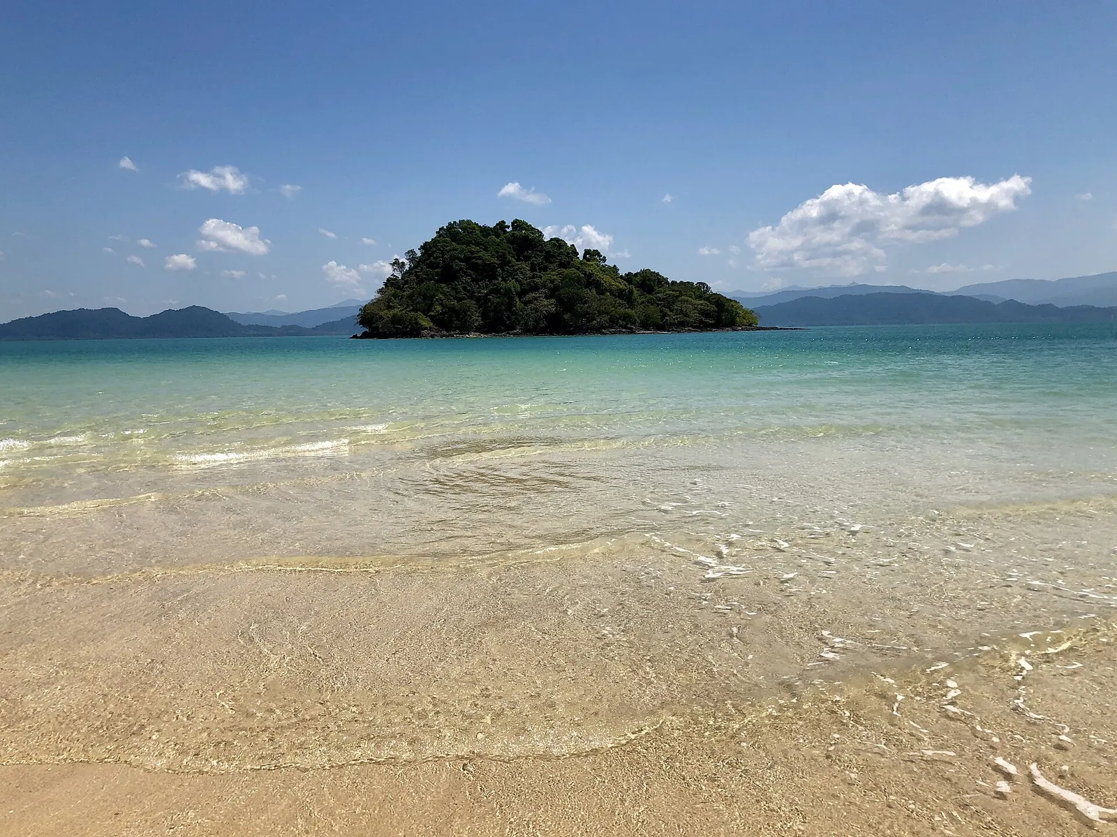 Clear shallow water and a wooded island off a sandy beach near Ranong