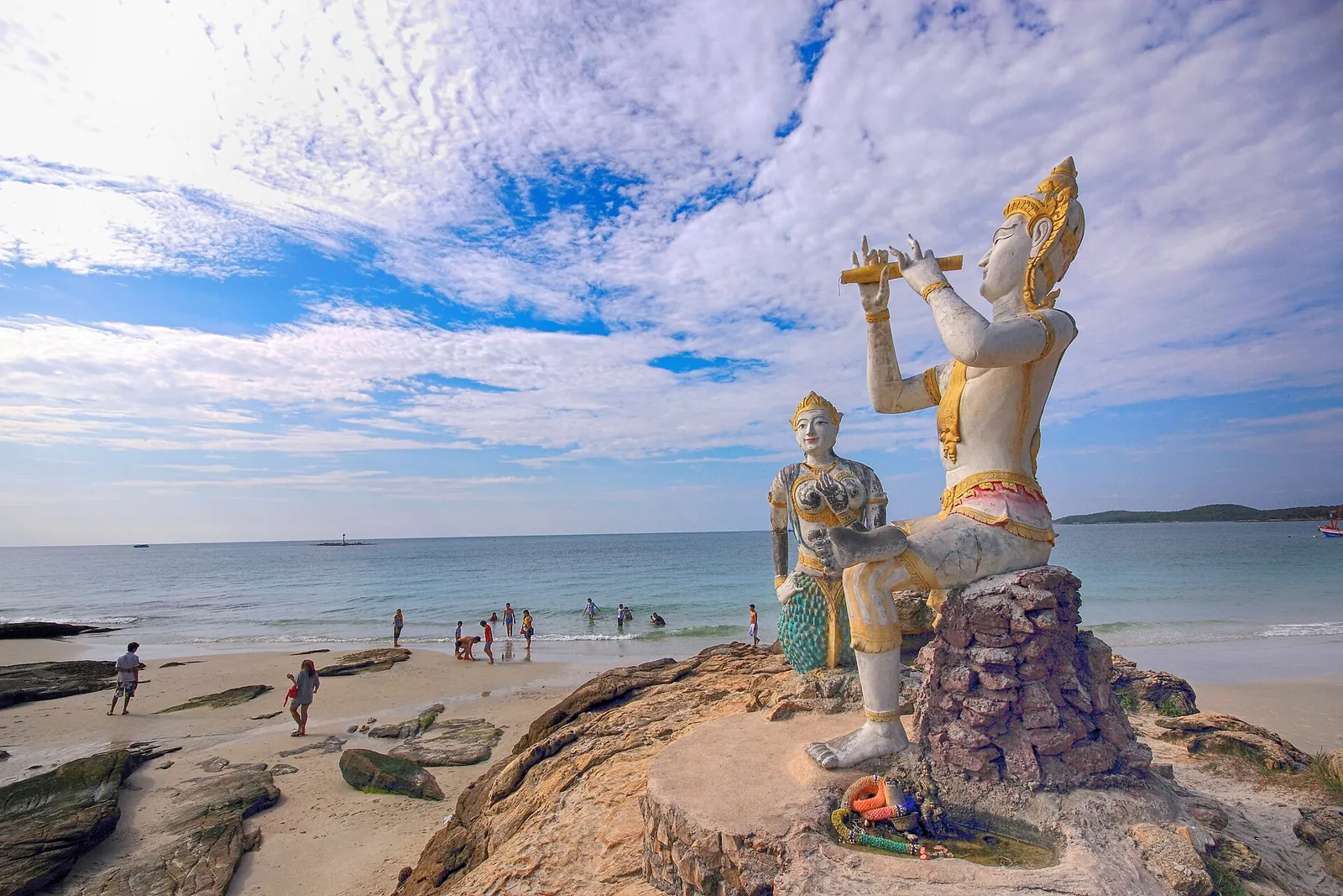 A statue of a mythical figure playing a flute on rocks by a Rayong beach