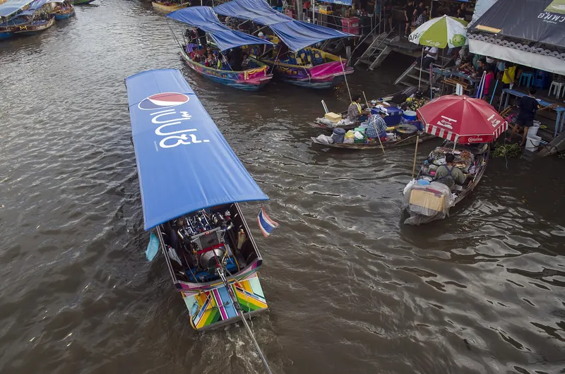 Longtail boats with blue canopies moving along the canal at Amphawa Floating Market