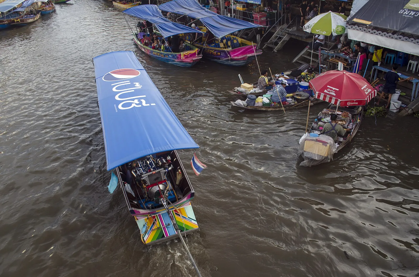 Longtail boats with blue canopies moving along the canal at Amphawa Floating Market