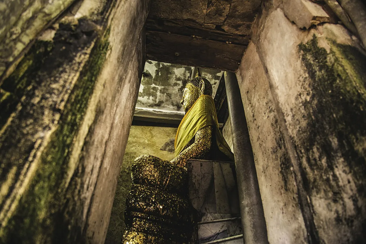 A gilded Buddha image inside the root-covered chapel of Wat Bang Kung