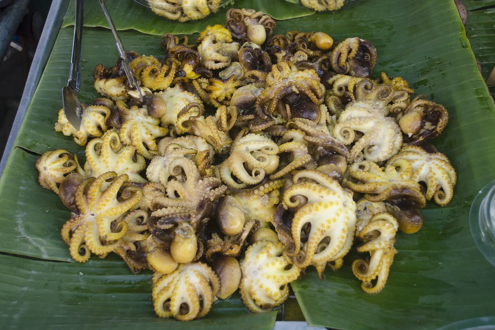 Grilled baby octopus piled on a banana leaf at a market stall