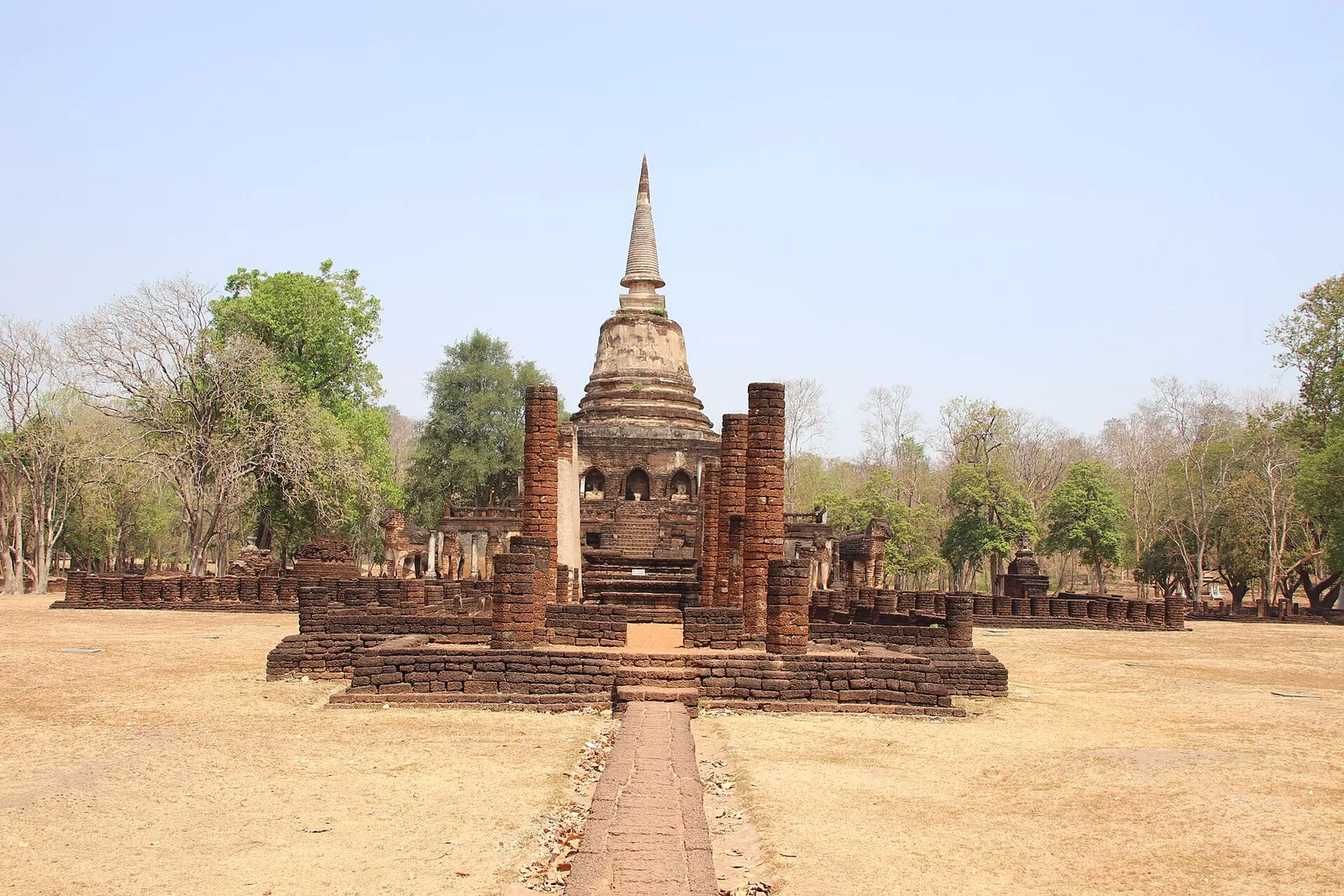 The bell-shaped chedi of Wat Chang Lom rising behind a brick walkway and ruined hall