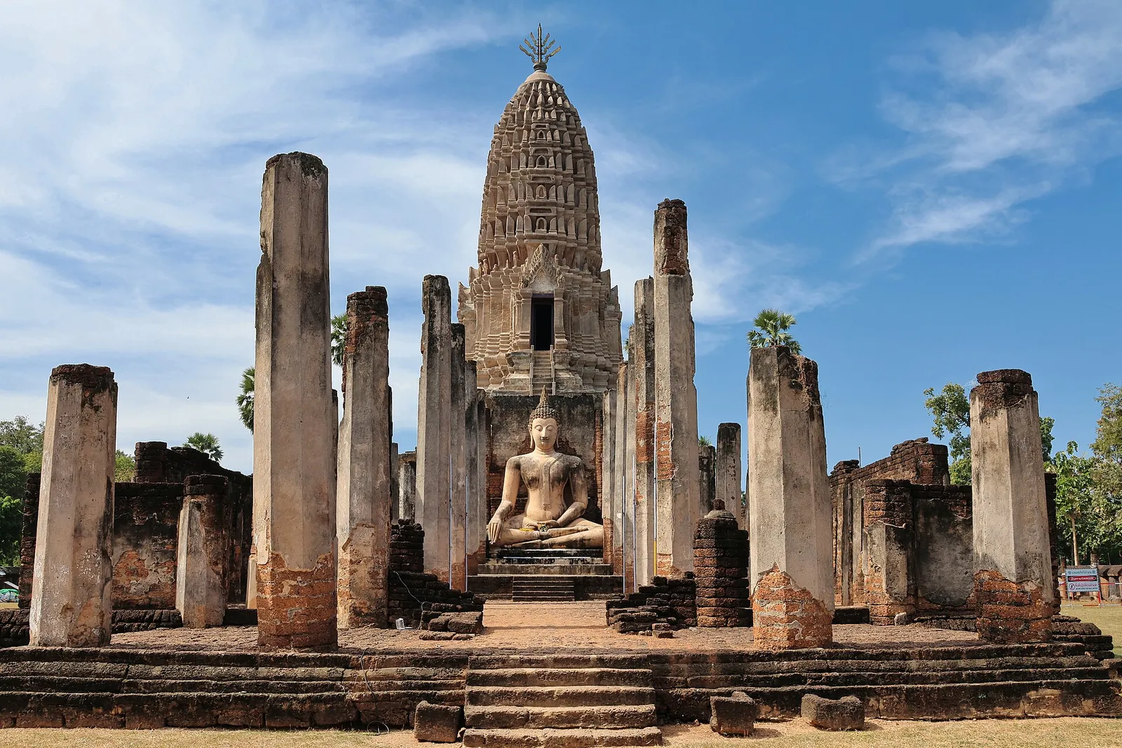 The laterite prang of Wat Phra Si Rattana Mahathat behind tall pillars and a seated Buddha