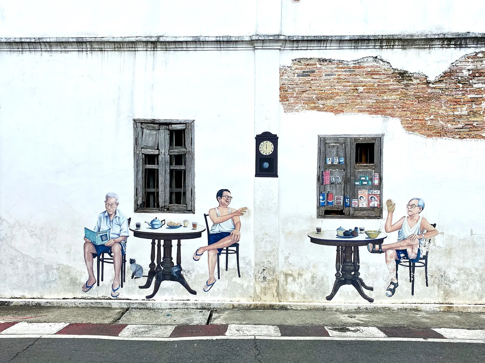 A street mural of old men drinking coffee painted on a whitewashed wall in Songkhla Old Town