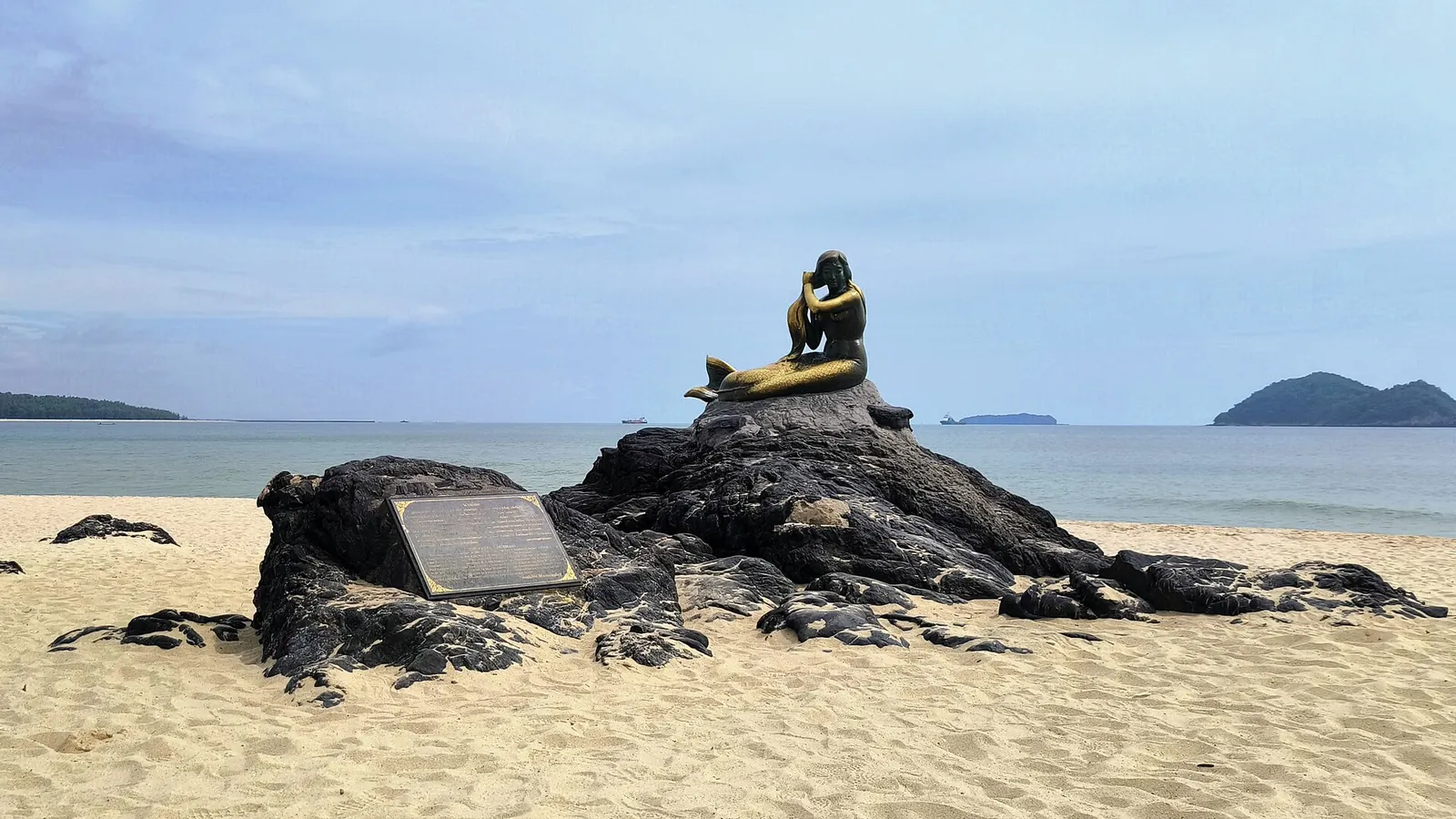 The Golden Mermaid statue on rocks at Samila beach with islands offshore