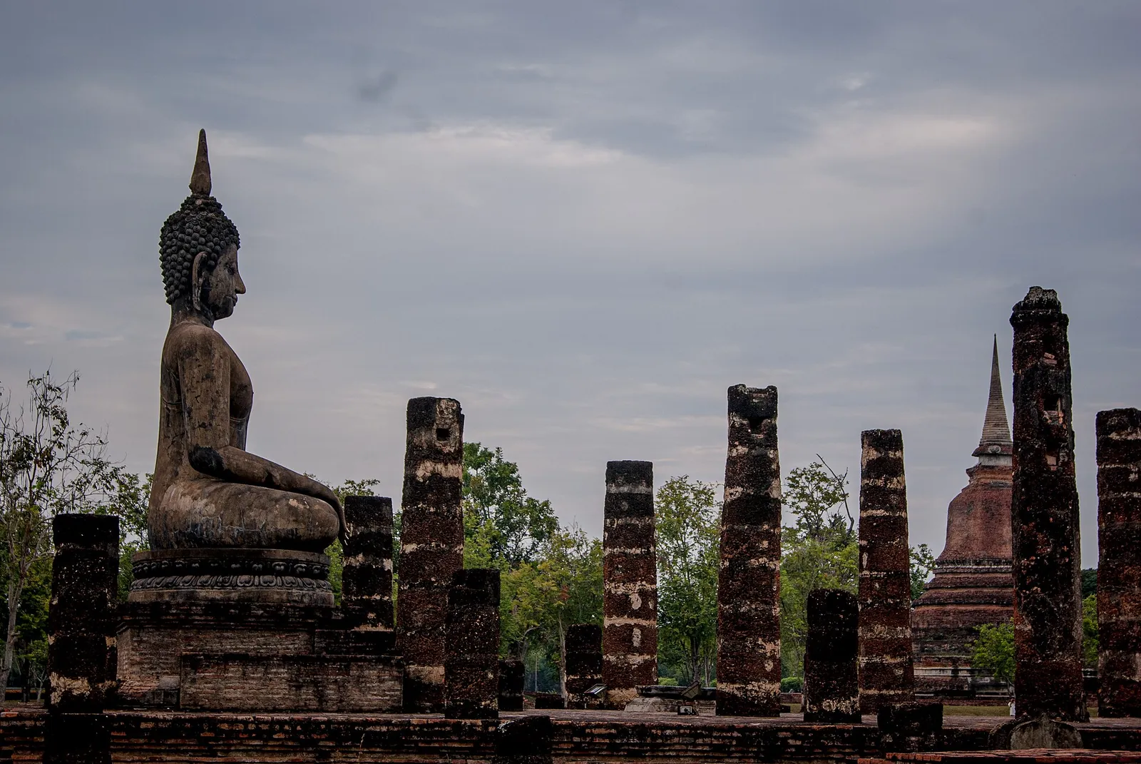 A seated Buddha beside rows of ruined laterite pillars at Wat Mahathat