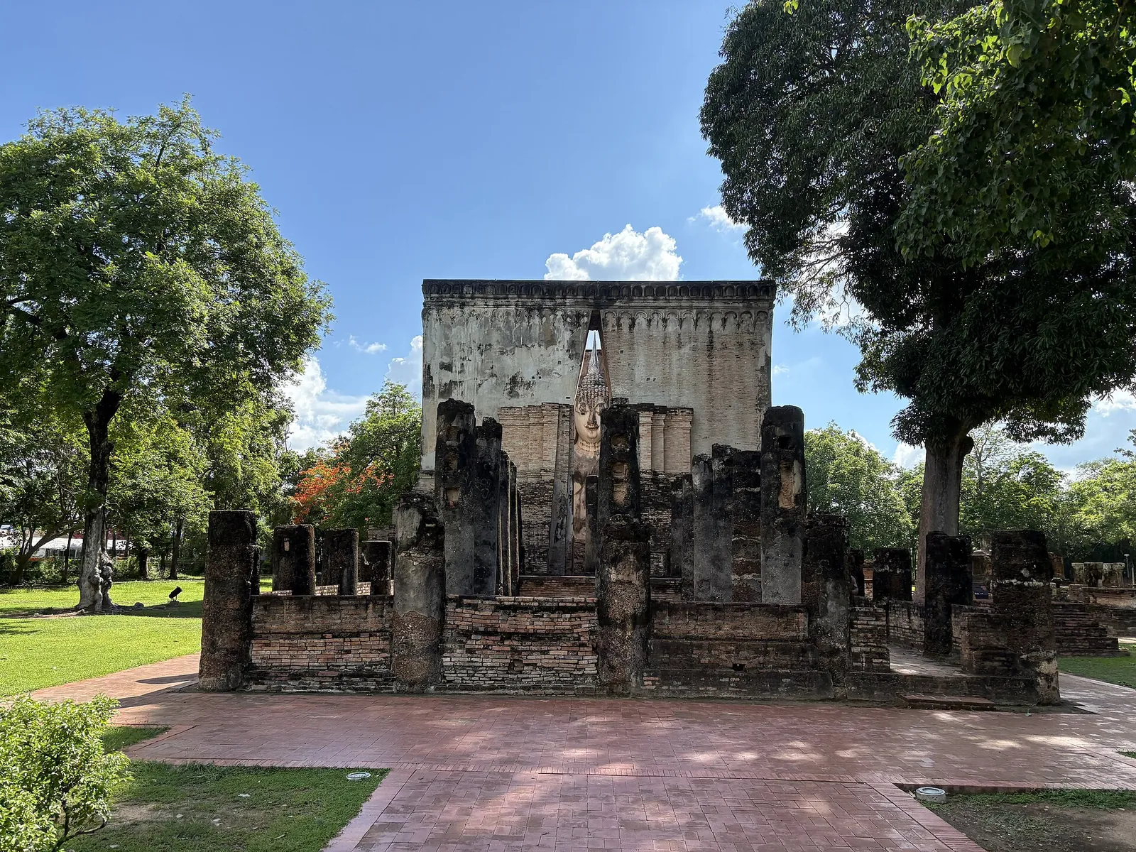 The square brick mondop of Wat Si Chum behind ruined walls under a blue sky