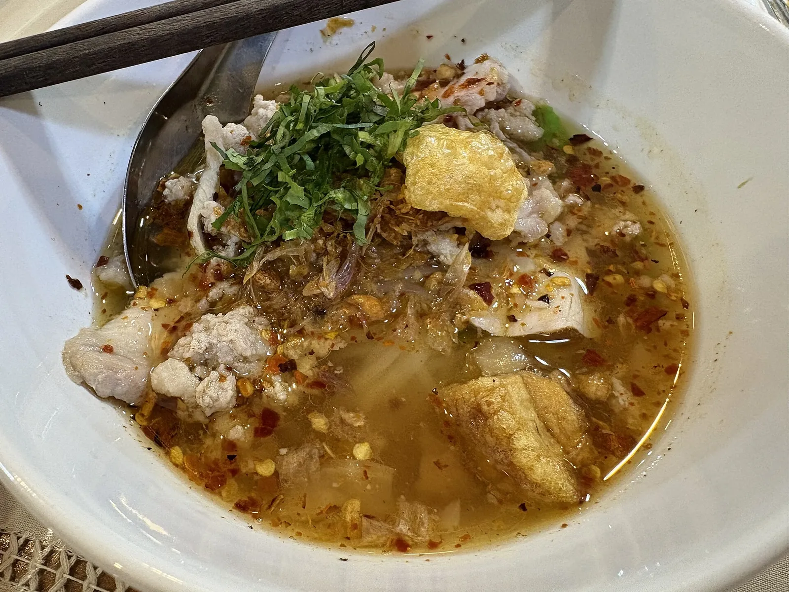A bowl of Sukhothai noodles with minced pork, crispy pork, herbs and chilli flakes
