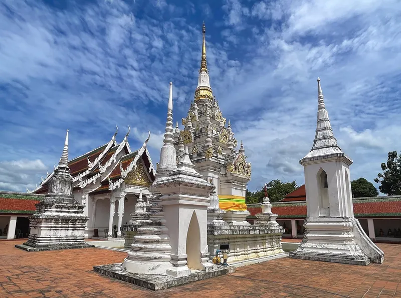 The ornate stucco-and-brick chedi of Wat Phra Borommathat Chaiya beside smaller white chedis