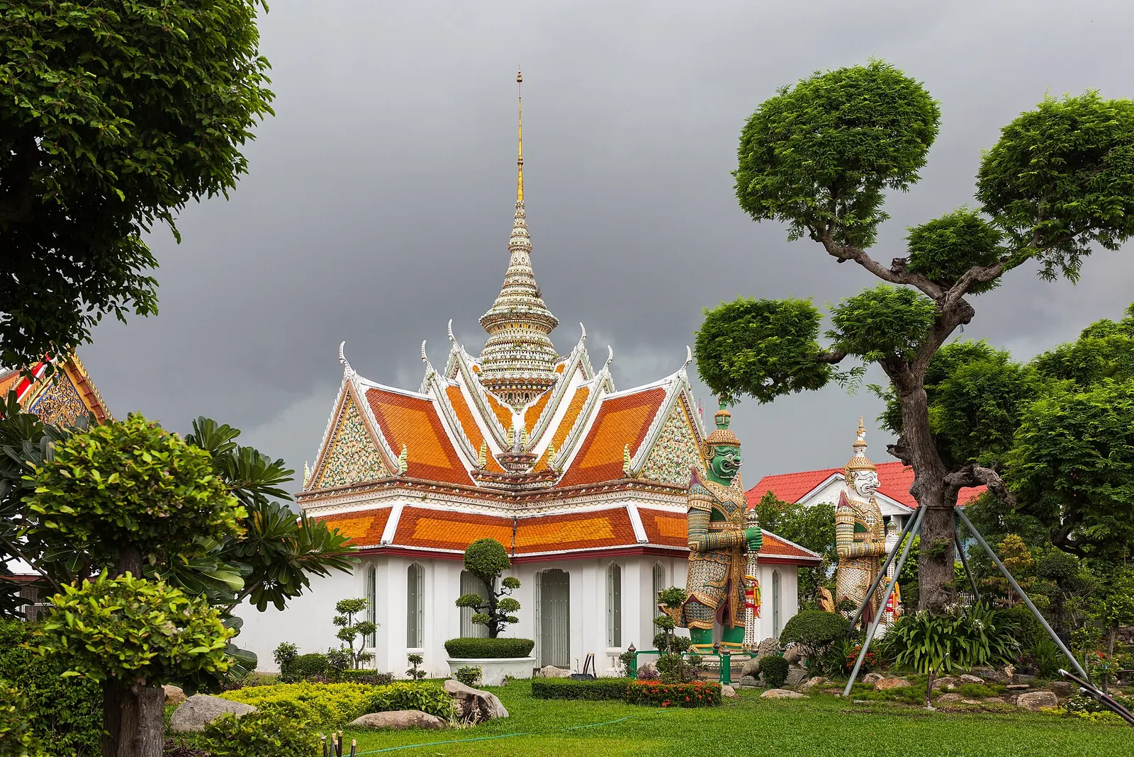 Bílé a oranžové střechy chrámů vedle ořezaných stromů ve Wat Arun v Bangkoku