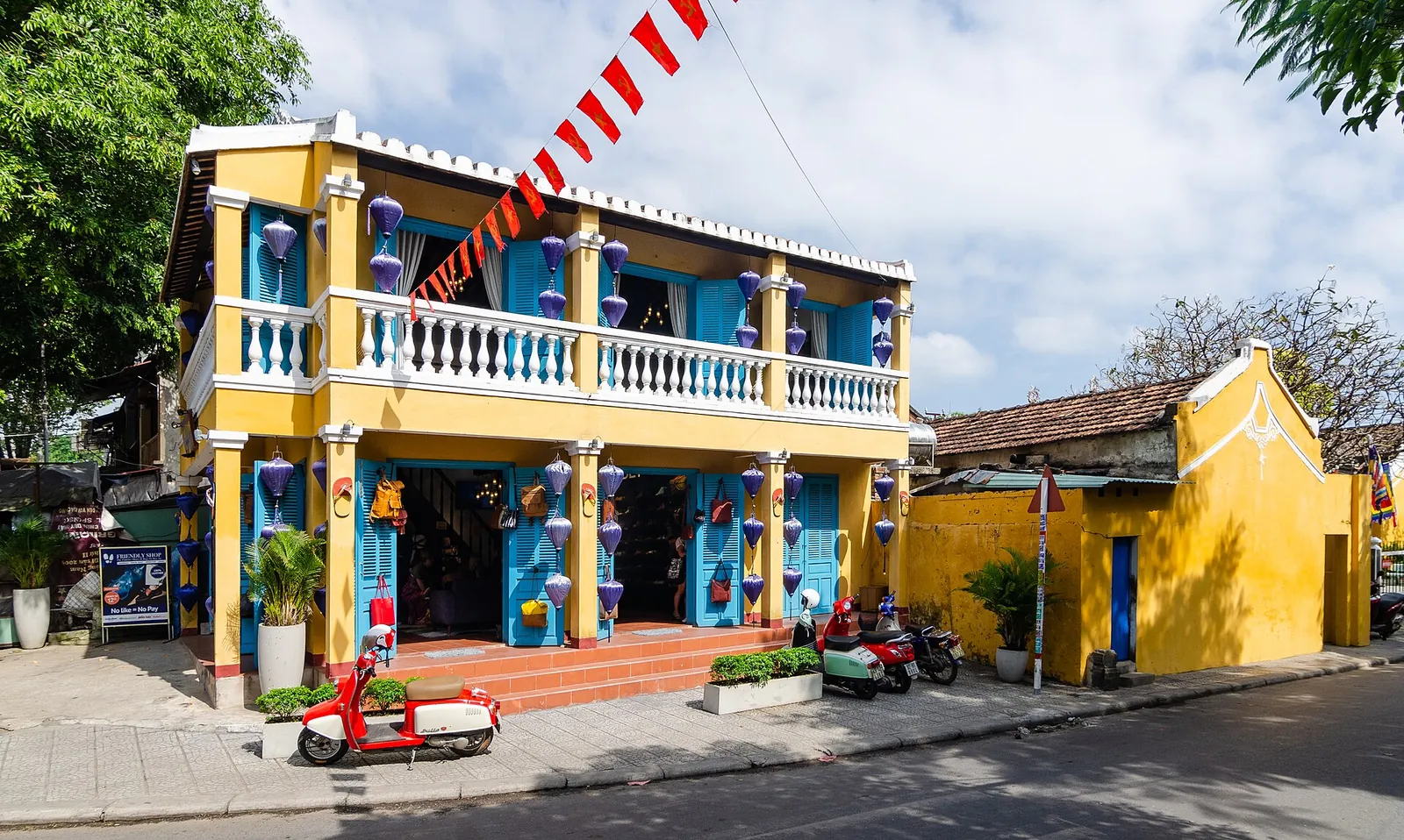 A yellow colonial-era house with blue shutters and a balcony on a corner of Hoi An's old town