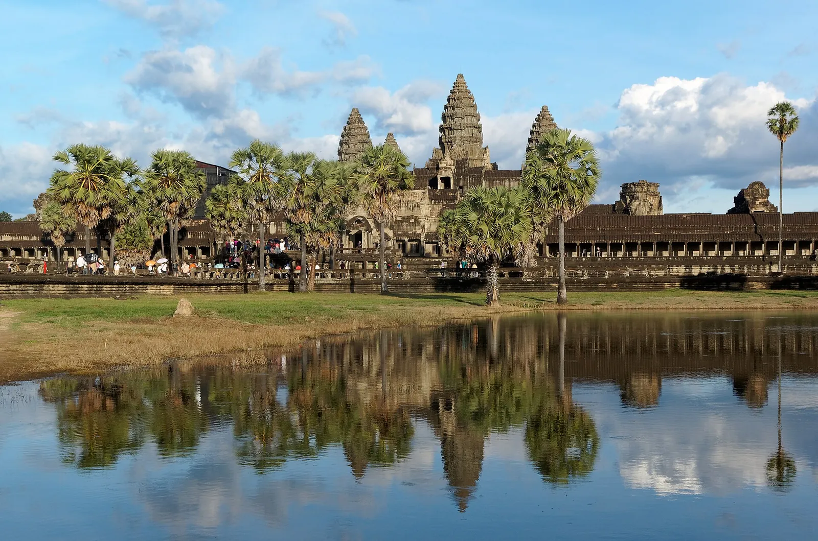 The towers of Angkor Wat behind palms, reflected in the pond in front of the temple