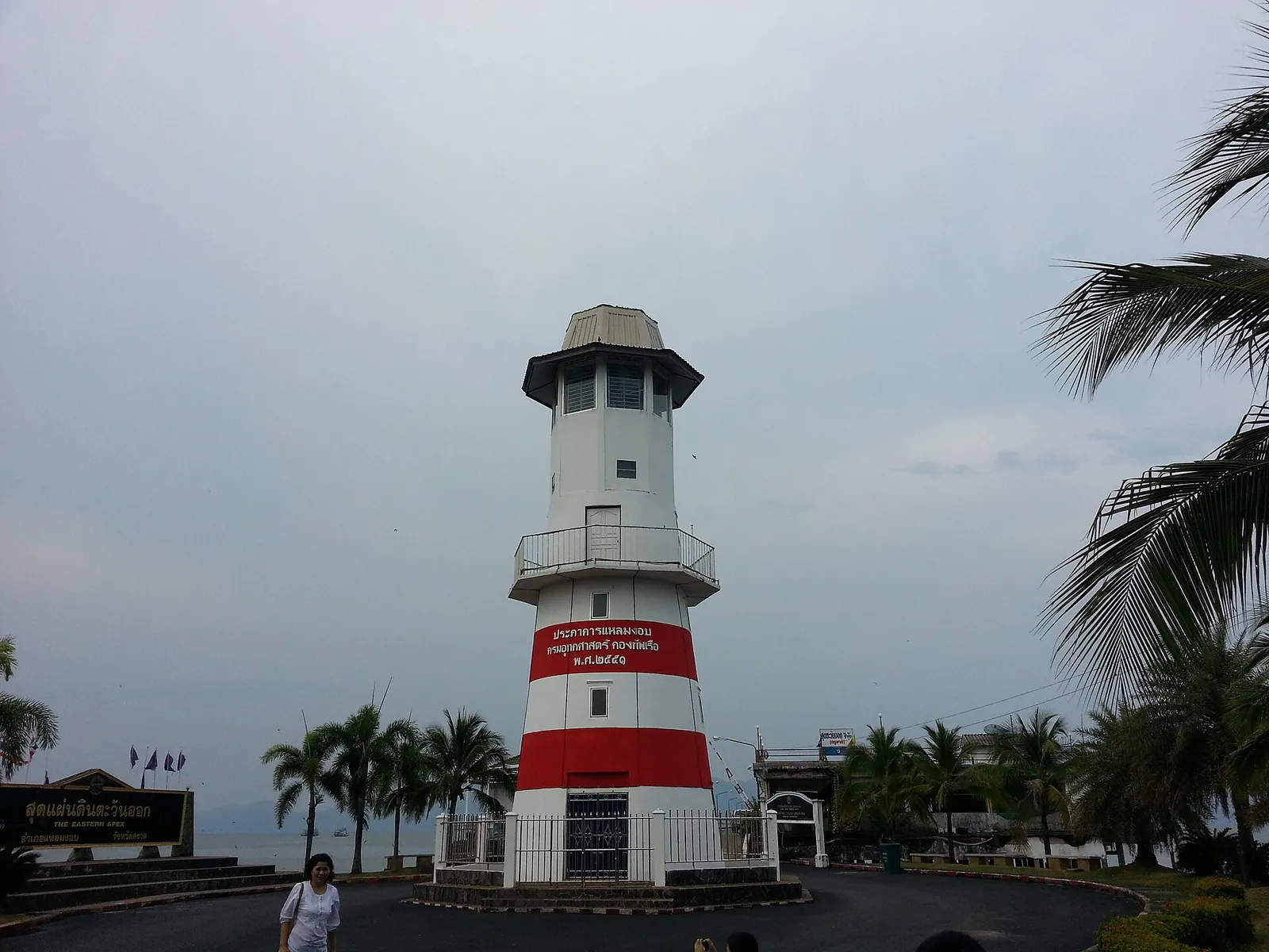 A red-and-white lighthouse at the Laem Ngop pier with palm trees