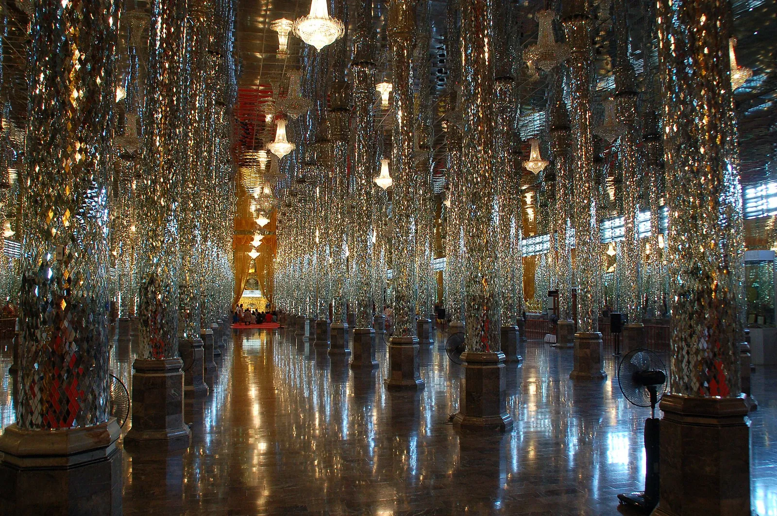 Una larga sala con columnas de cristal espejado y lámparas de araña en Wat Tha Sung