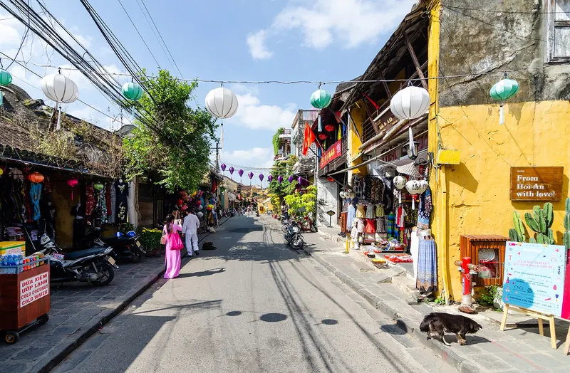 Flat street in Hoi An Ancient Town lined with yellow shophouses and paper lanterns under a blue sky