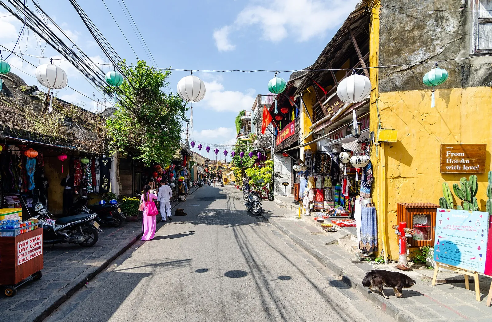 Flat street in Hoi An Ancient Town lined with yellow shophouses and paper lanterns under a blue sky
