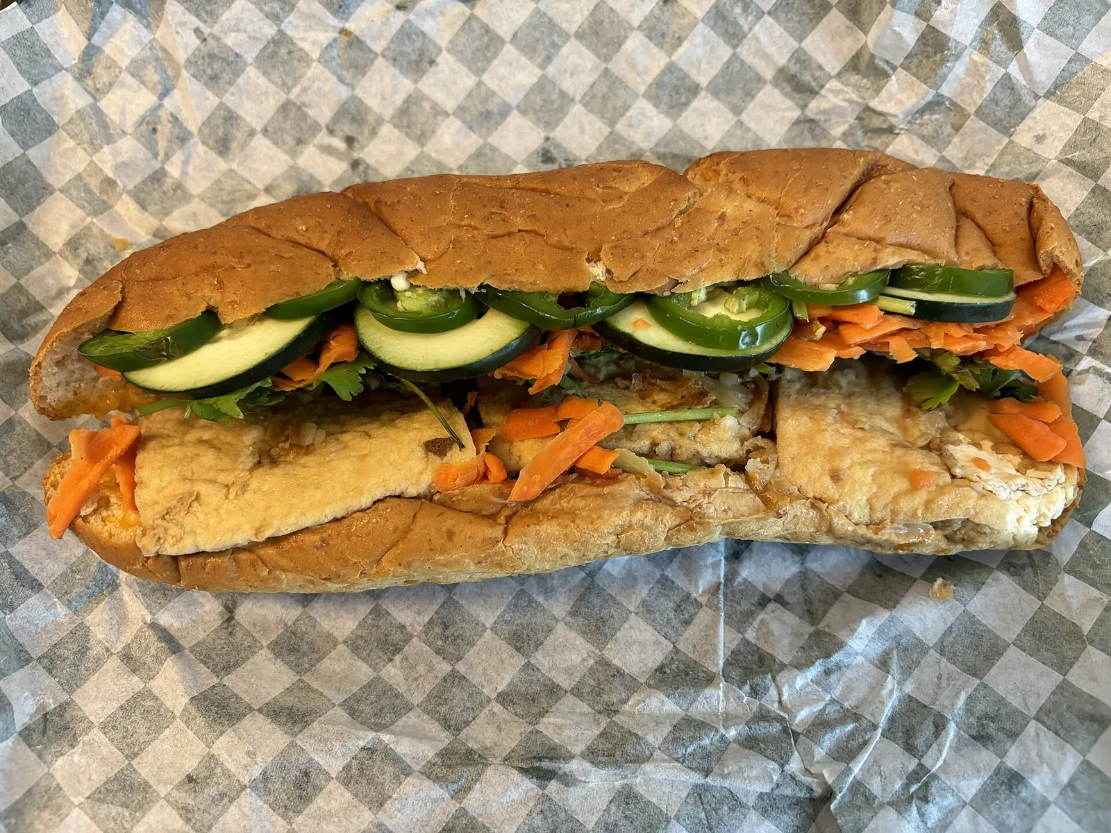 A tofu bánh mì baguette filled with tofu, cucumber, carrot and chilli on a paper wrapper