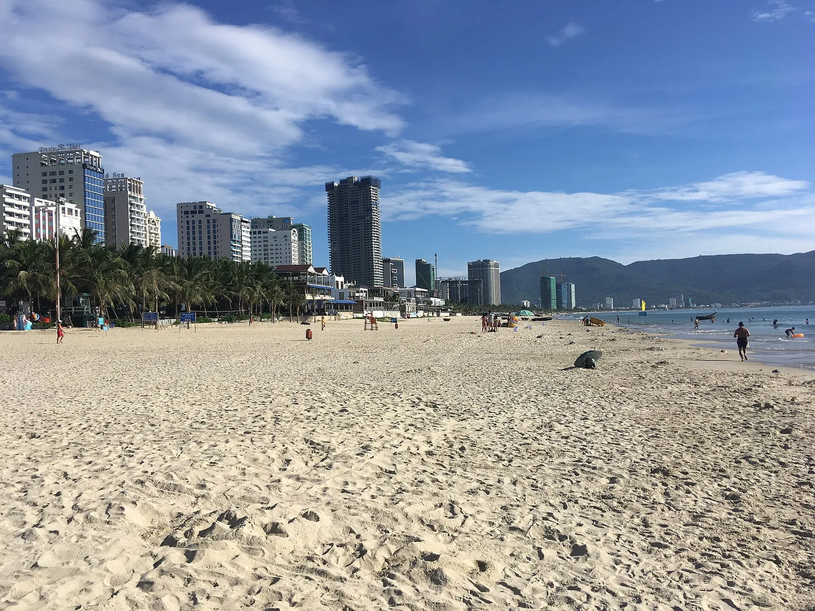 Wide sandy My Khe Beach in Da Nang with high-rise buildings behind the palms