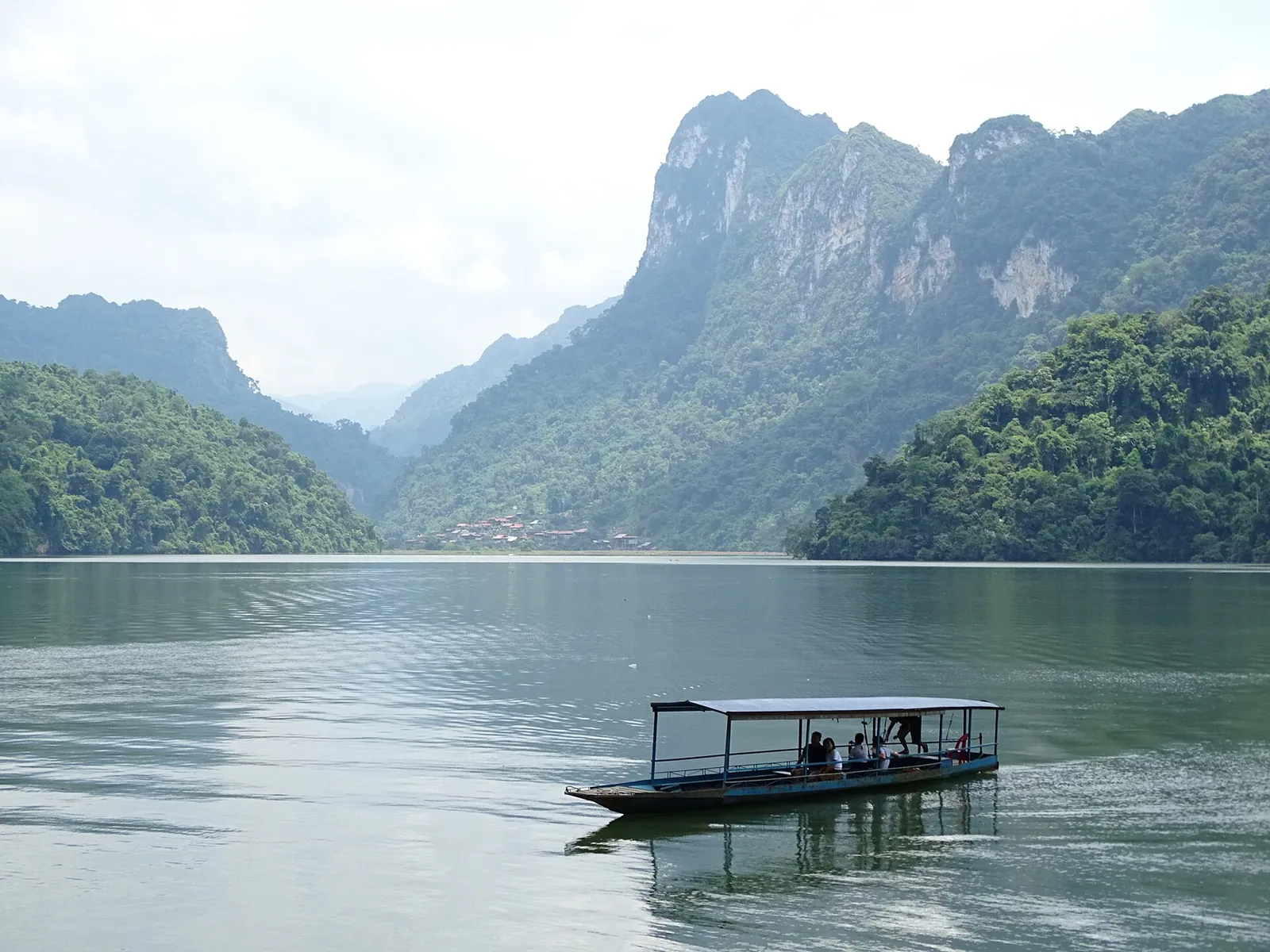 A small passenger boat crossing Ba Be Lake below forested limestone cliffs
