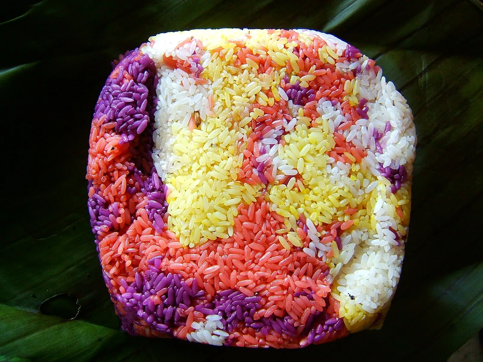 A mound of five-colour sticky rice in purple, red, yellow and white on a banana leaf