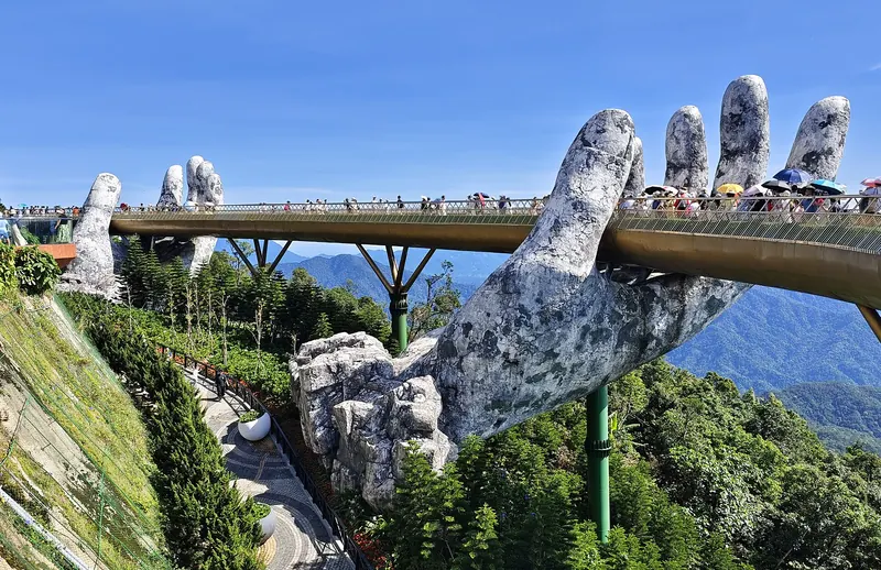 The Golden Bridge at Ba Na Hills, a curving gold walkway held up by two giant stone-textured hands above forested slopes