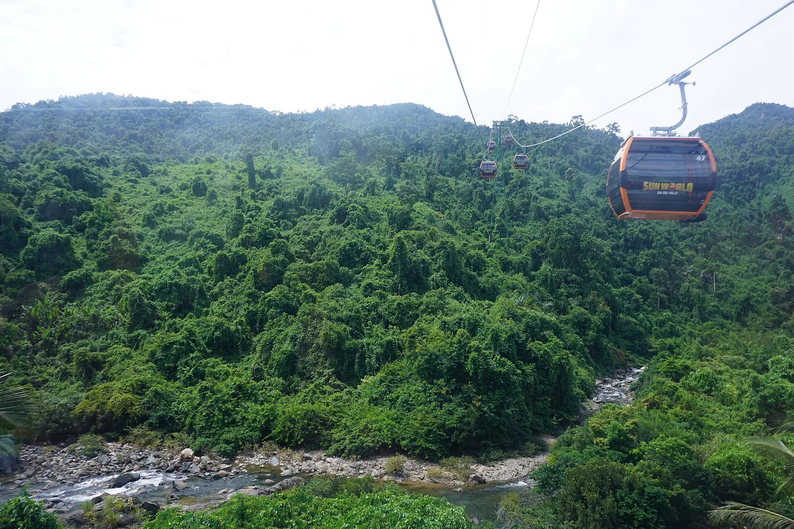 A Ba Na Hills cable car cabin crossing dense green forest above a mountain stream