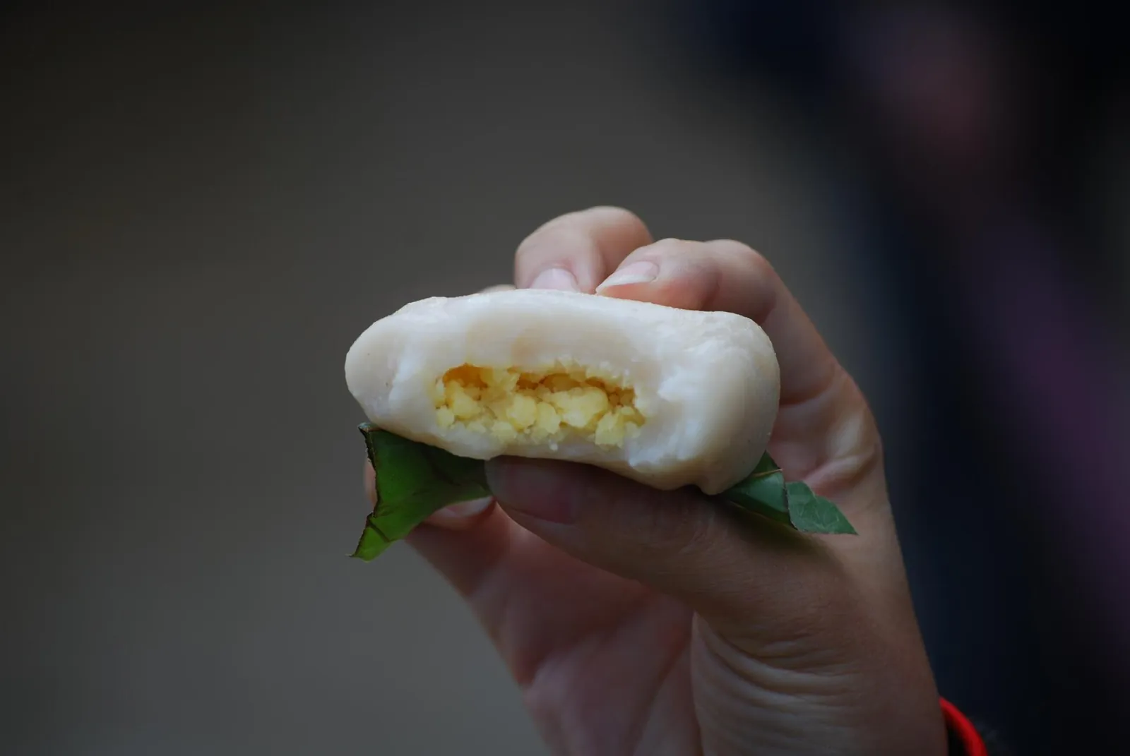 A hand holding a round white glutinous rice cake split open to show a yellow mung bean filling