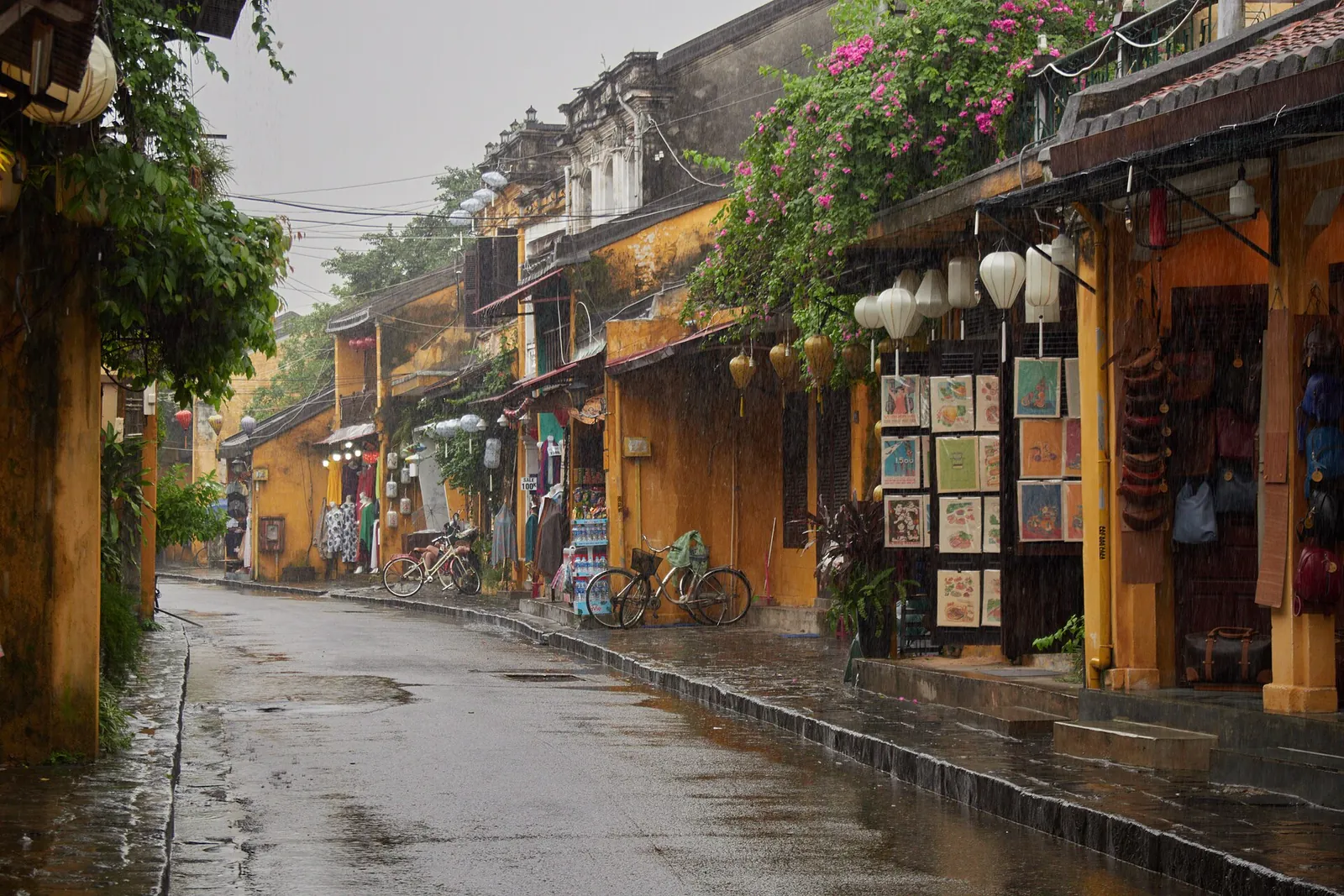 A rain-wet, empty street of yellow shophouses in Hoi An Ancient Town under a grey sky