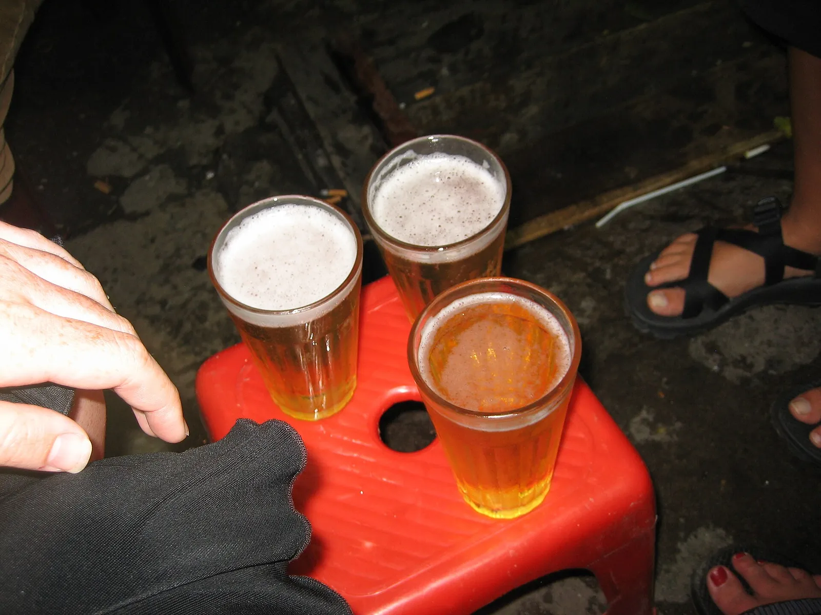 Three glasses of bia hoi, fresh draught beer, on a red plastic stool at a Hanoi street bar