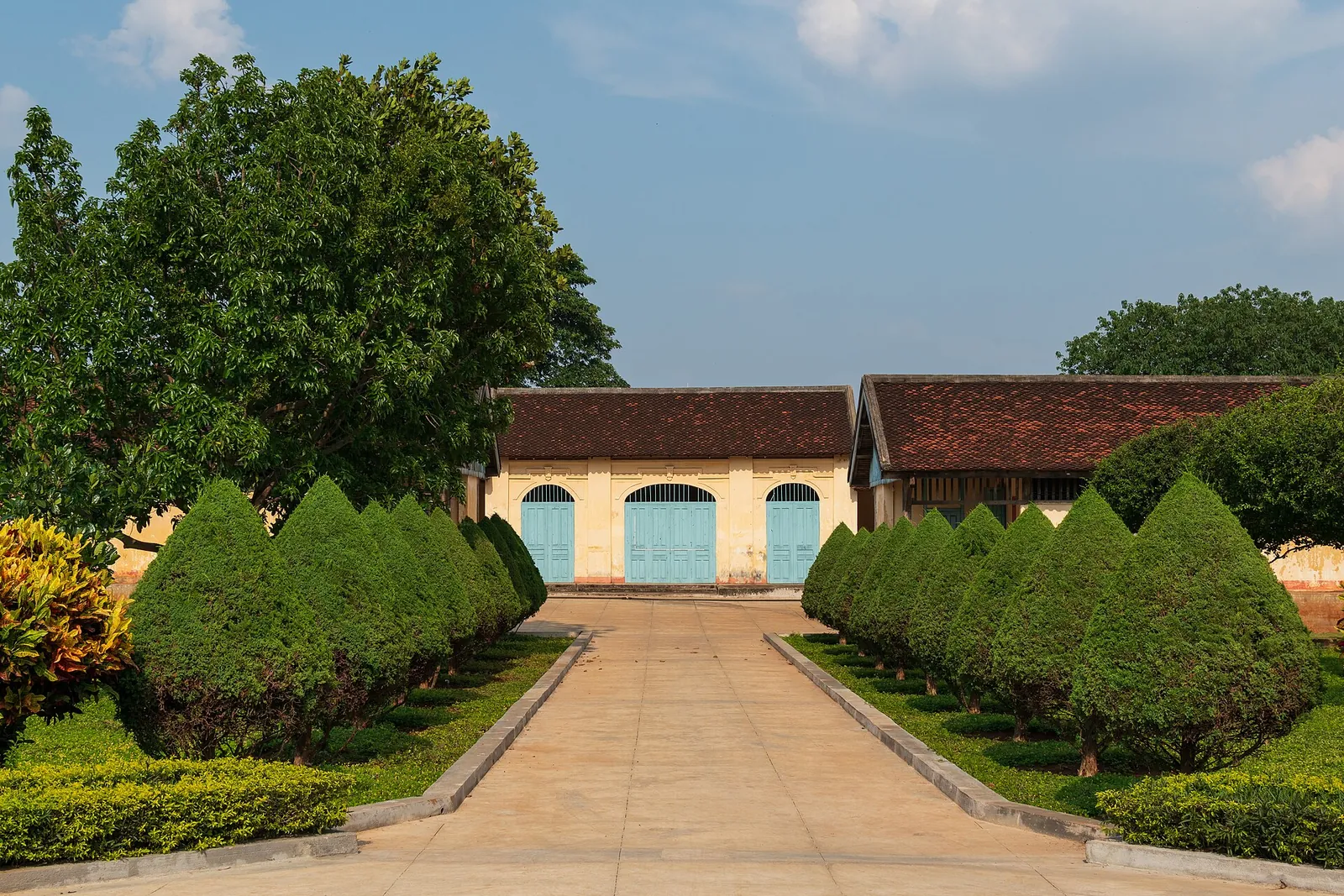 Garden path lined with clipped shrubs leading to yellow colonial buildings at the Buon Ma Thuot Exile House