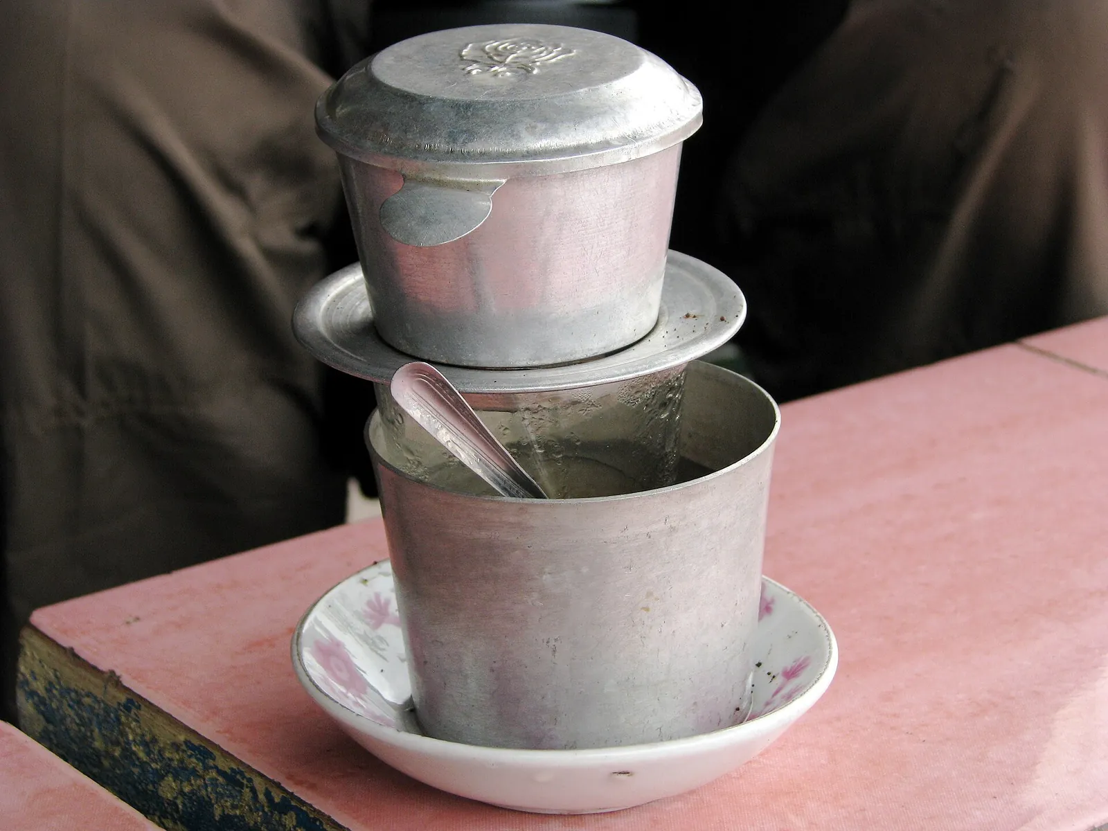 Glass of Vietnamese coffee dripping through a metal phin filter
