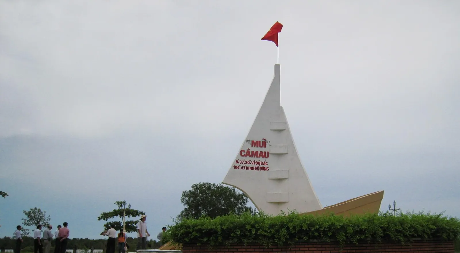 White boat-shaped monument with a red flag at Cape Ca Mau, with visitors in front