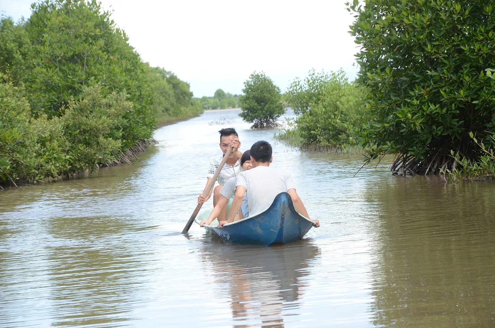Two visitors paddling a small boat along a channel between mangroves and a shrimp pond in Nam Can