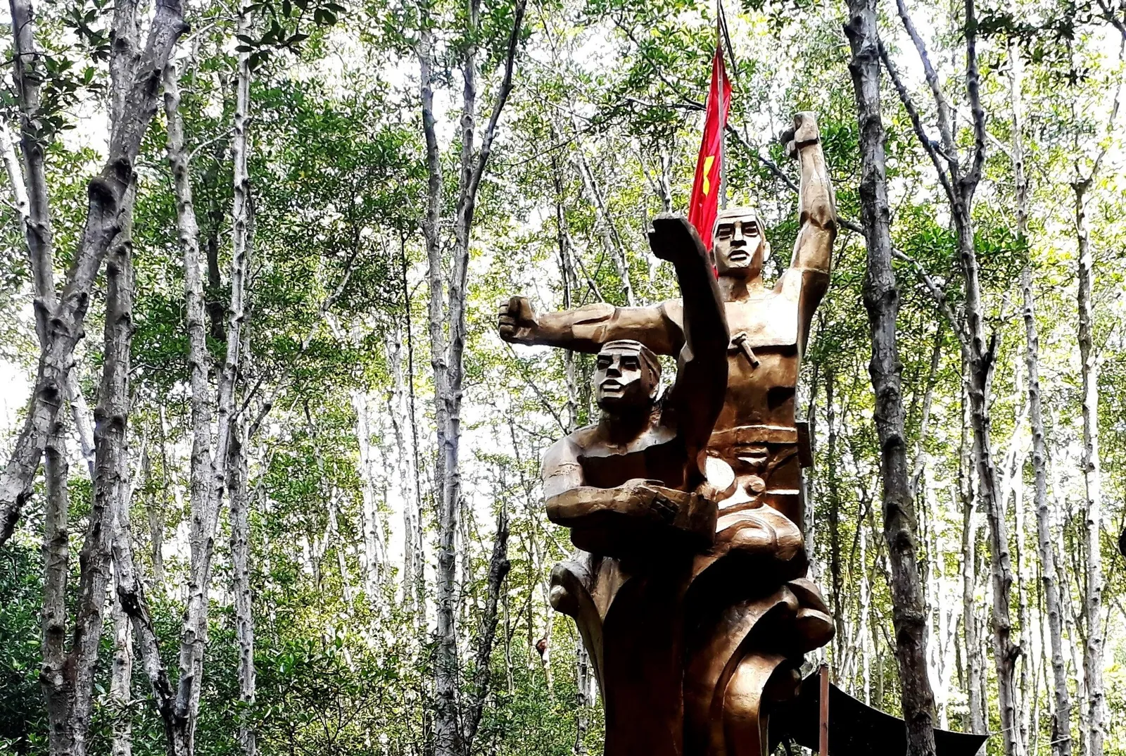 Bronze statue of special-forces fighters raising a flag among mangrove trunks at the Rung Sac base