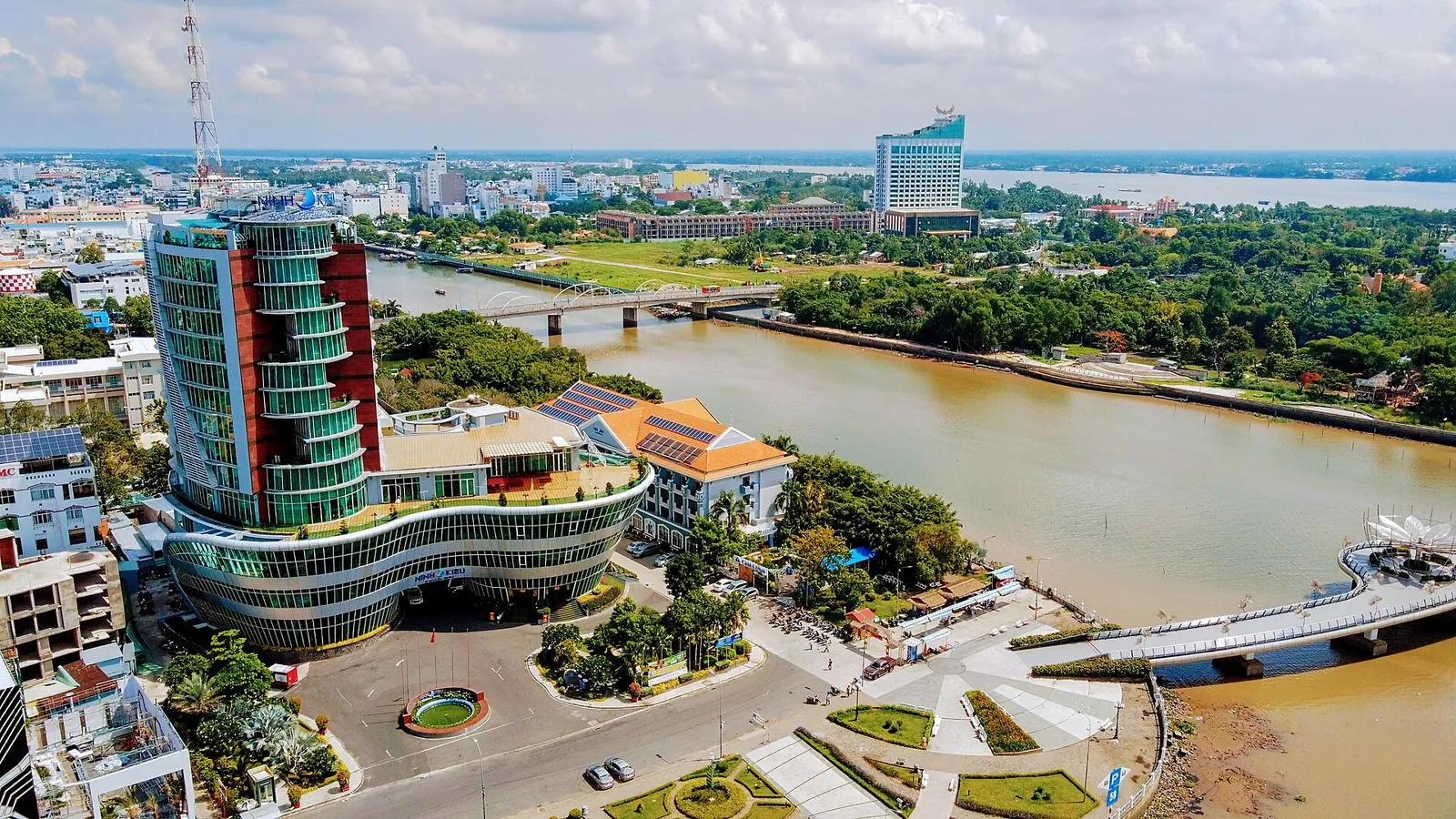Aerial view of central Can Tho with a curved glass high-rise, riverside gardens and the wide Can Tho River curving past the city