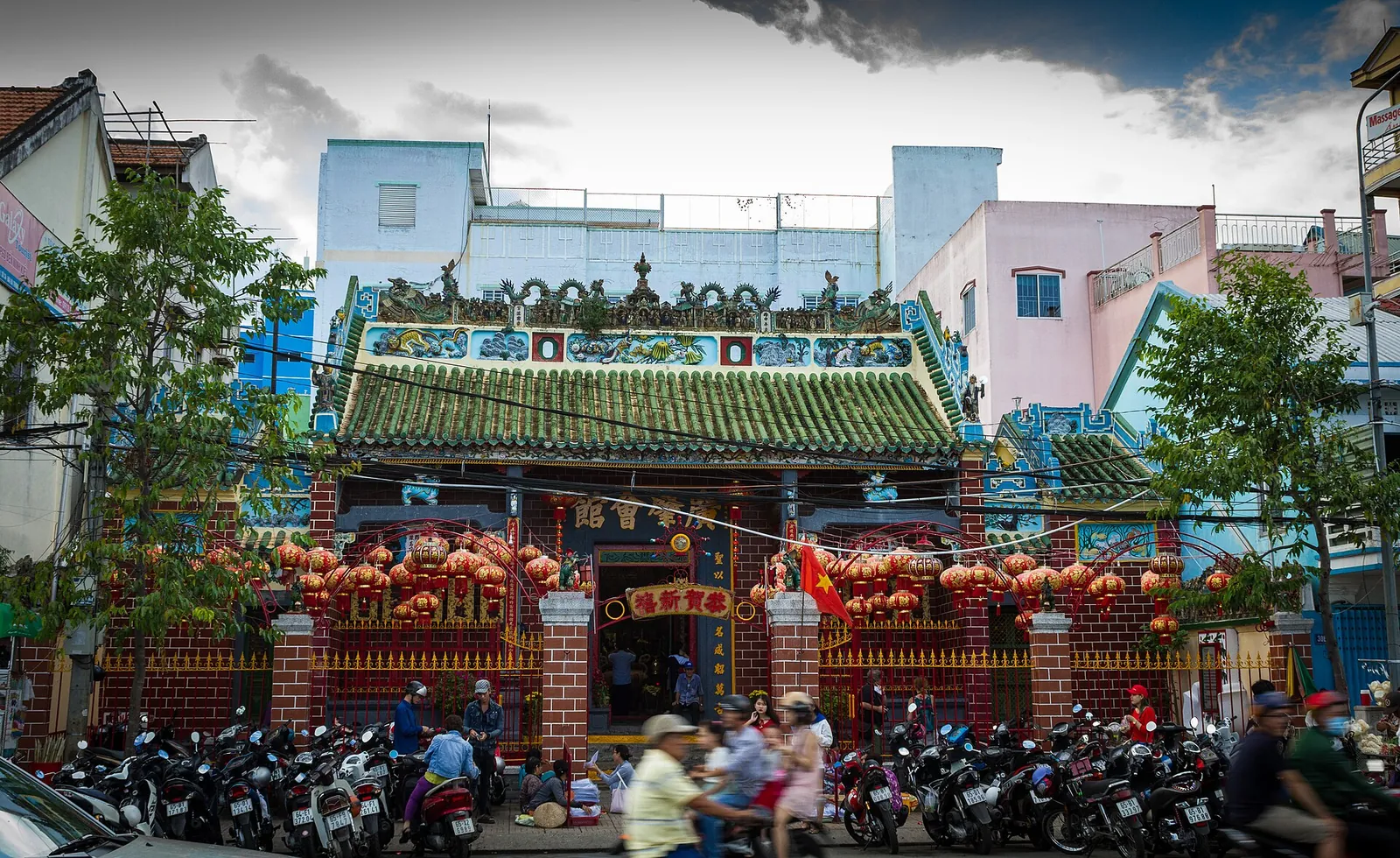 Ornate Chinese temple front with a green-tiled roof, red lanterns and motorbikes parked outside on the street in Can Tho