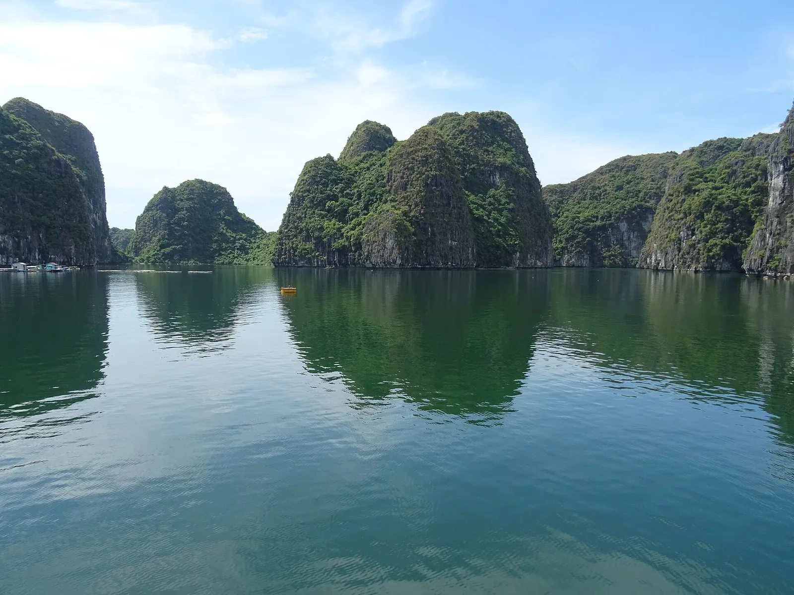 Green limestone islands reflected in calm water in Lan Ha Bay under a blue sky