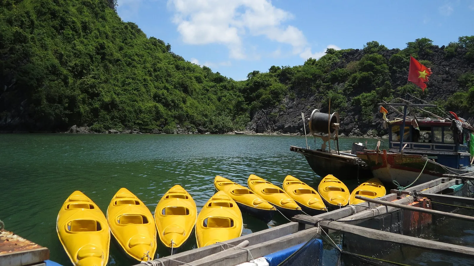 A row of yellow kayaks moored by a jetty on Lan Ha Bay with forested karst behind