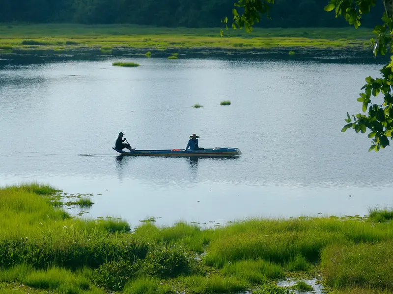 Two people in a small boat on Crocodile Lake (Bau Sau) surrounded by green marsh grass in Cat Tien National Park
