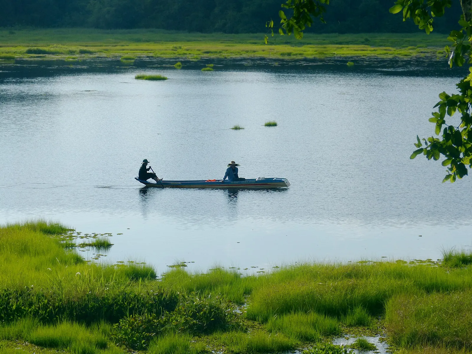 Two people in a small boat on Crocodile Lake (Bau Sau) surrounded by green marsh grass in Cat Tien National Park