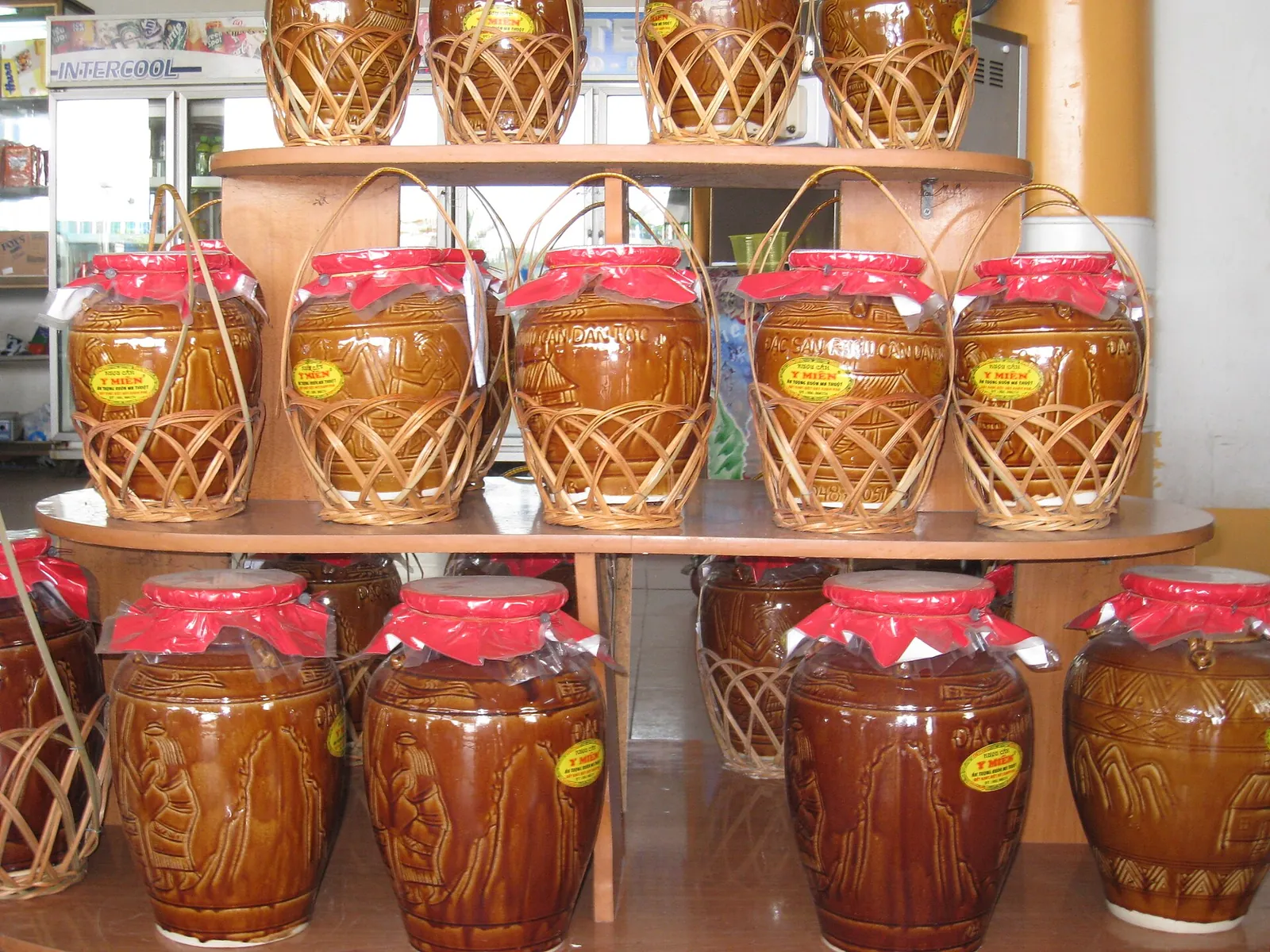 Rows of rượu cần rice-wine jars in woven baskets on shelves in a shop