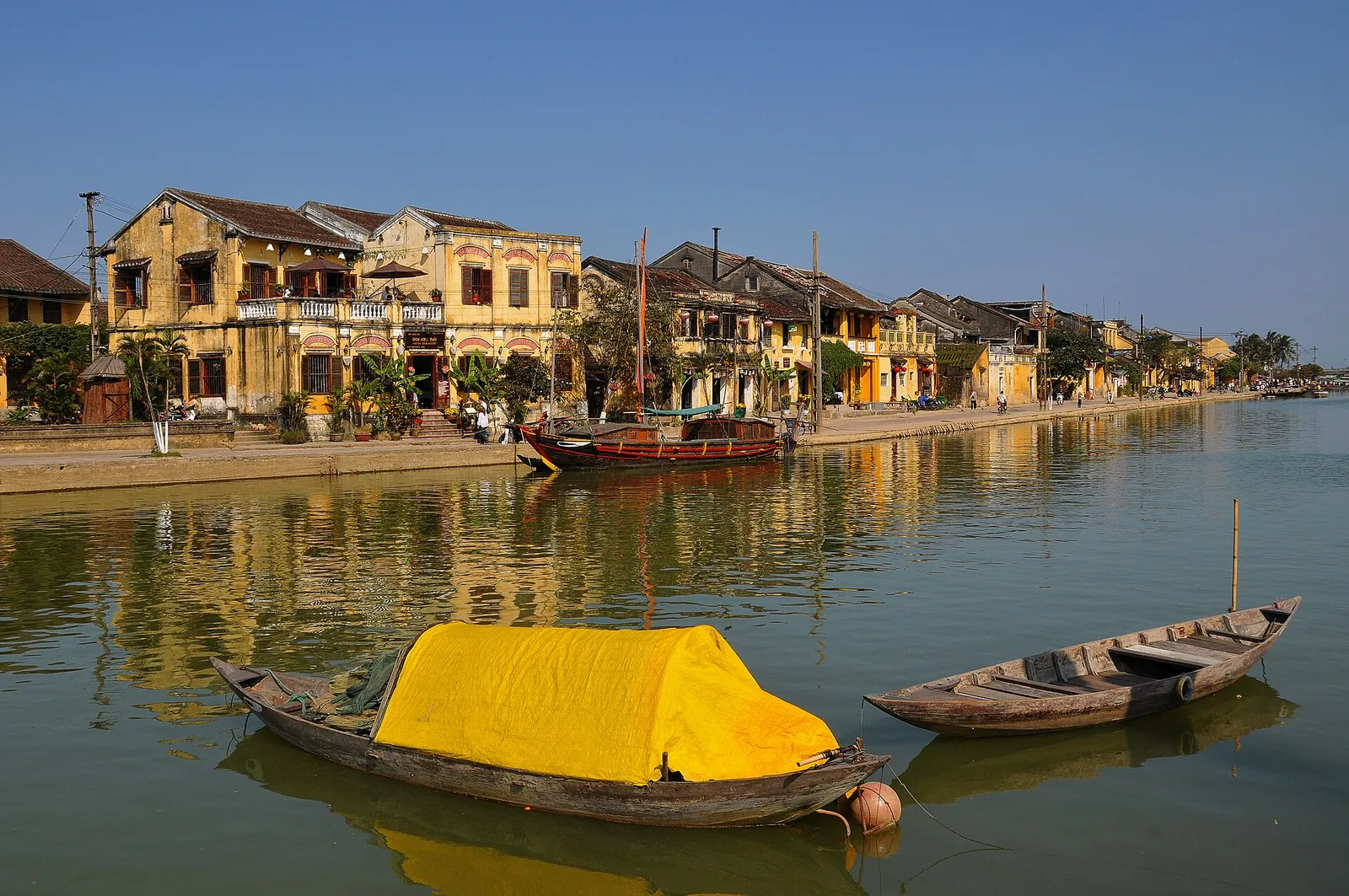 Yellow shophouses along the Hoi An waterfront with wooden boats moored on the Thu Bon River