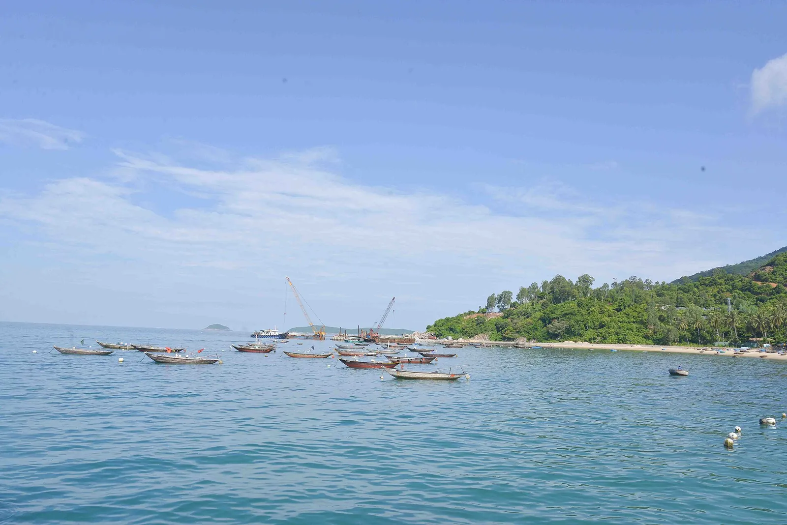 Fishing boats moored in a turquoise bay below a green hillside at Bai Huong, Cham Islands